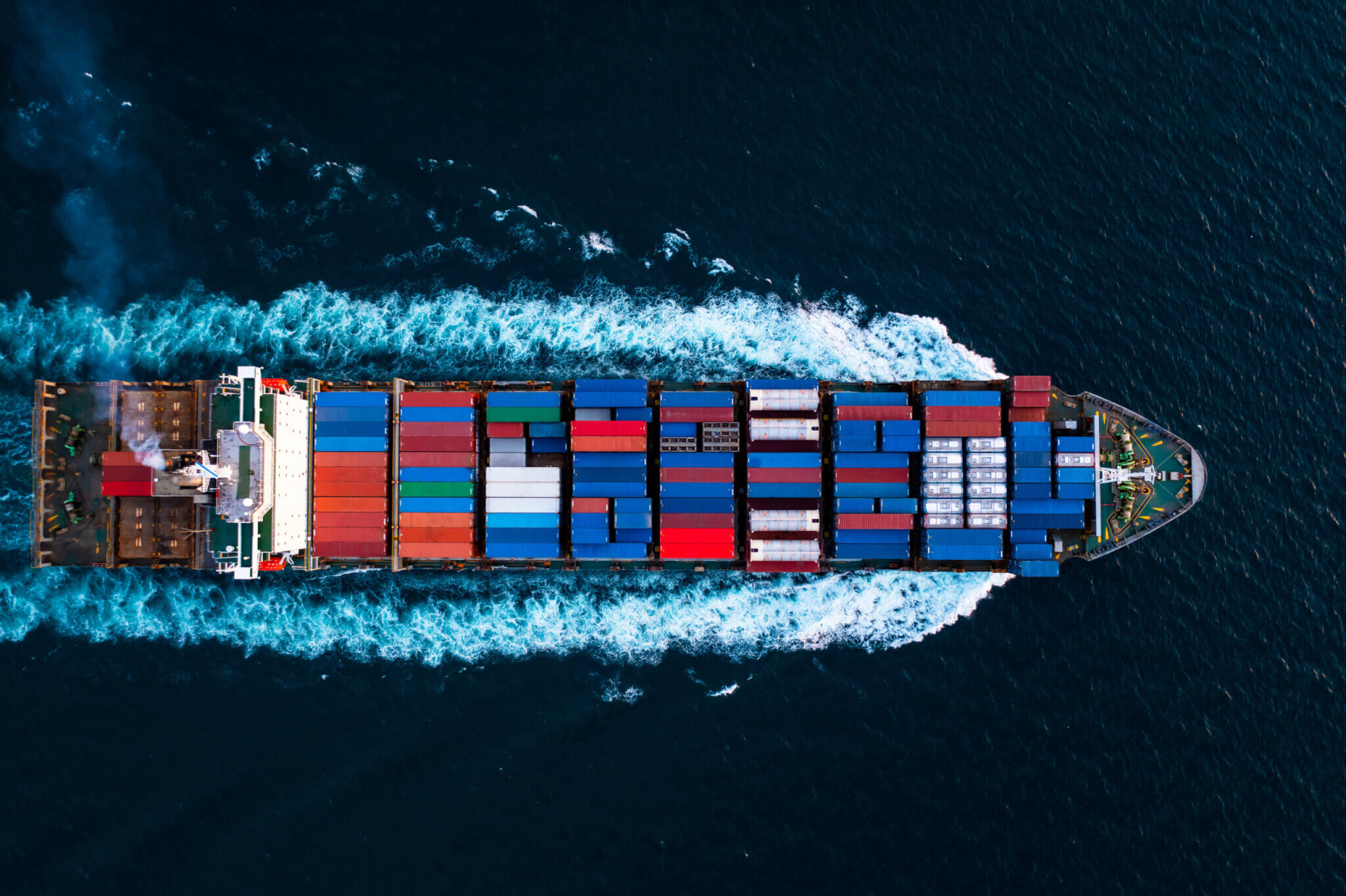 A top-down view of a large container ship on its journey at sea surrounded by deep blue water.