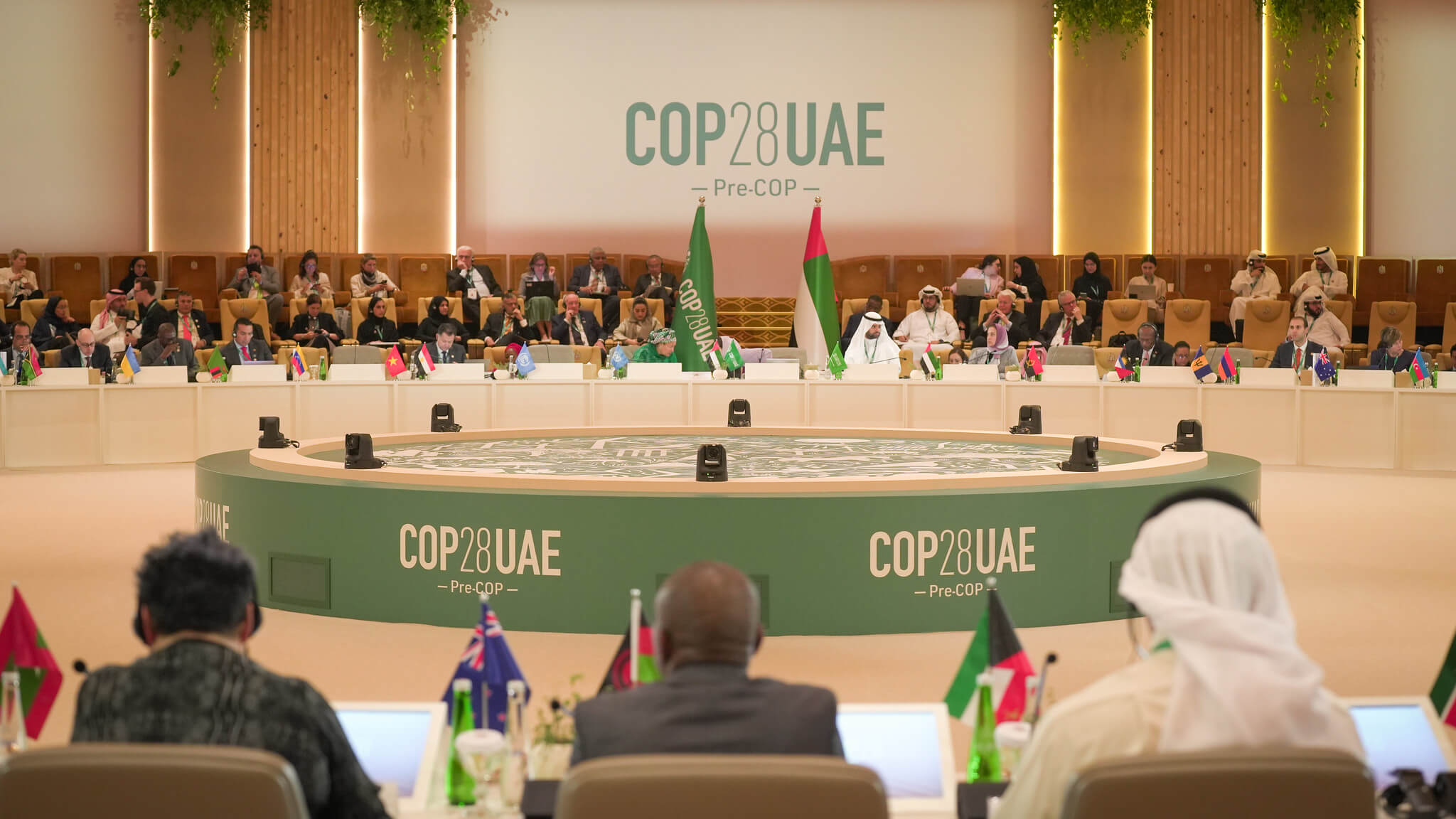 Global delegates sit in a round white room, with signs reading COP28 UAE.